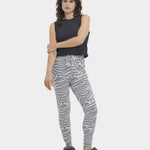 A woman standing, wearing high-waisted drawstring pants with a cloudy grey and white stripe pattern, paired with a black top and black footwear. Available at Be Charmed
