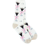 A pair of World's Softest white crew socks with a repeating pattern of black cocktail glasses tied with pink bows, featuring beige heels and toes, displayed on a clean white background. Available at Be Charmed