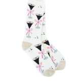 A pair of World's Softest white crew socks with a repeating pattern of black cocktail glasses tied with pink bows, featuring beige heels and toes, displayed on a clean white background. Available at Be Charmed