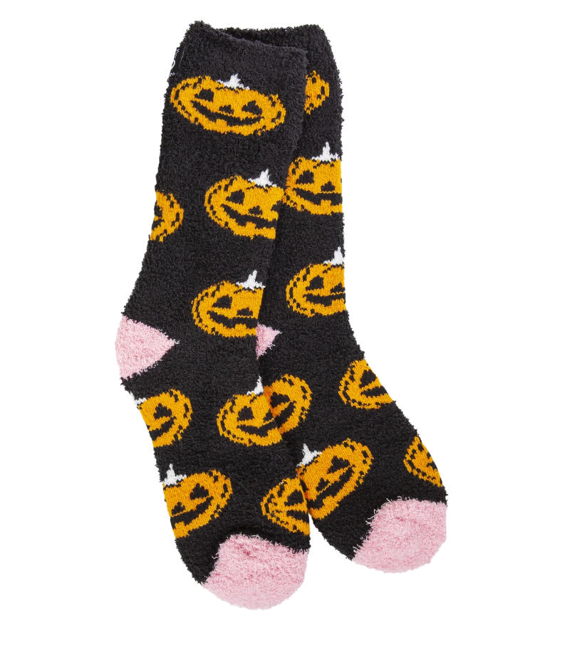 A pair of black fuzzy socks with an all-over orange jack-o'-lantern pattern, featuring pink heels and toes, shown on a plain white background. Available at Be Charmed