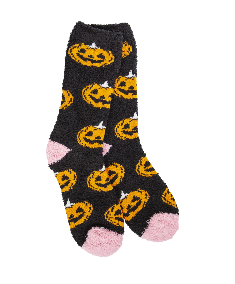A pair of black fuzzy socks with an all-over orange jack-o'-lantern pattern, featuring pink heels and toes, shown on a plain white background. Available at Be Charmed