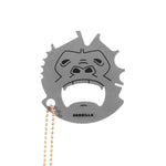 A stainless steel grill scraper with a monkey-like face design and a small chain attached to it. The brand 'GRRILLA' is inscribed on the scraper. Available at Be Charmed