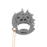 A stainless steel grill scraper with a monkey-like face design and a small chain attached to it. The brand 'GRRILLA' is inscribed on the scraper. Available at Be Charmed
