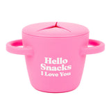 A bright pink siliconeBella Tunno  snack cup with a lid and side handles, featuring the white text 'Hello Snacks I Love You' and 'BELLA TUNNO' on the front, set against a plain white background. Available at Be Charmed