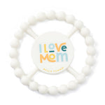 A white silicone baby teether with a circular beaded ring and a central round insert that reads 'I Love Mom' in colorful lettering, with 'BELLA TUNNOP' printed below. Available at Be Charmed