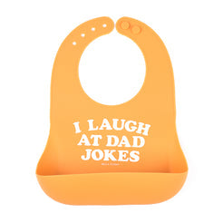 An orange Bella Tunno silicone baby bib with white printed text that reads 'I LAUGH AT DAD JOKES' on a solid white background. Available at Be Charmed