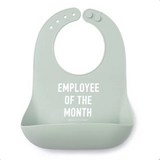 A light sage green Bella Tunno silicone baby bib with white text reading 'EMPLOYEE OF THE MONTH' and a small 'BRICK BRICK COMPANY' logo below, shown on a plain white background. Available at Be Charmed