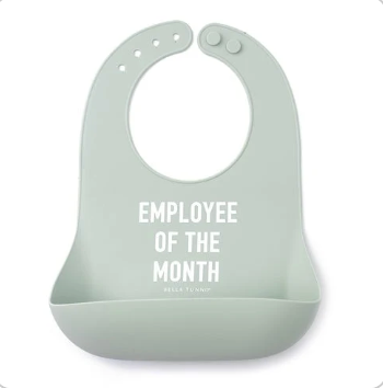 A light sage green Bella Tunno silicone baby bib with white text reading 'EMPLOYEE OF THE MONTH' and a small 'BRICK BRICK COMPANY' logo below, shown on a plain white background. Available at Be Charmed
