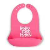 A bright pink Bella Tunno silicone baby bib with a white printed text design that reads 'Hello food I <heart> you' on a clean white background. Available at Be Charmed