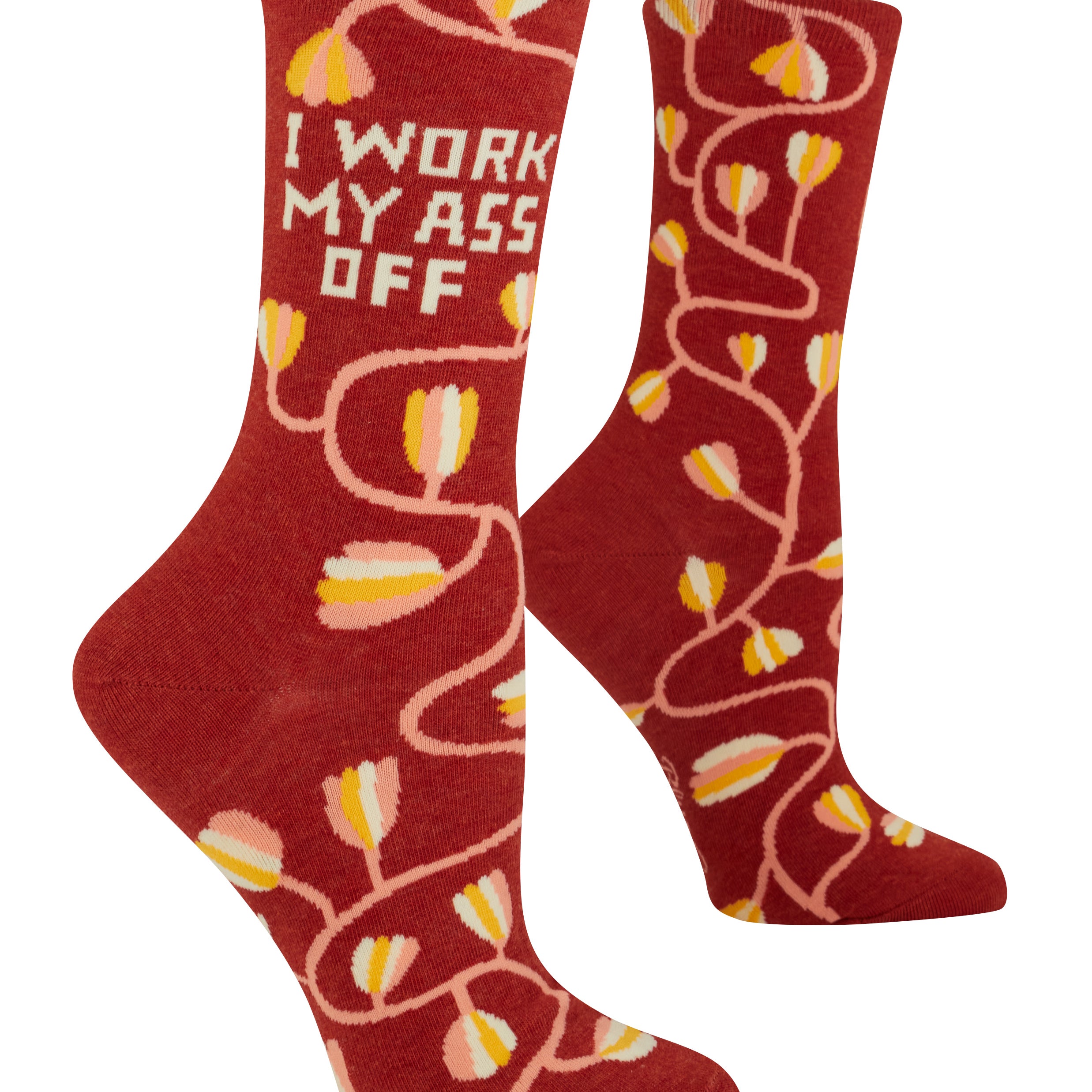 Red socks with yellow tulip pattern and text 'I WORK MY ASS OFF' on a white background. Available at Be Charmed