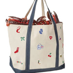 Back of an Alice & Wonder off-white canvas tote bag with navy blue trim and handles, decorated with colorful embroidered lobster-themed motifs including a lobster, red sock, blue cleats, and cherries. The bag is shown filled with lobsters against a light gray background. Available at Be Charmed