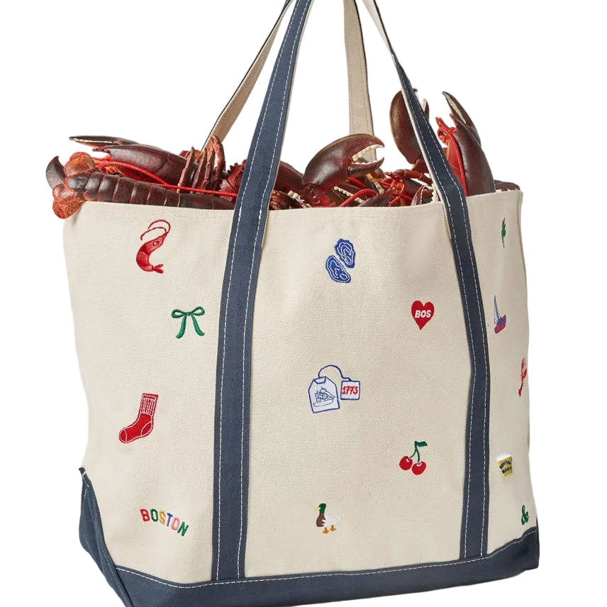 Back of an Alice & Wonder off-white canvas tote bag with navy blue trim and handles, decorated with colorful embroidered lobster-themed motifs including a lobster, red sock, blue cleats, and cherries. The bag is shown filled with lobsters against a light gray background. Available at Be Charmed