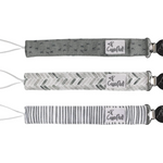 Three patterned pacifier clips on a white background, featuring different designs. Available at Be Charmed