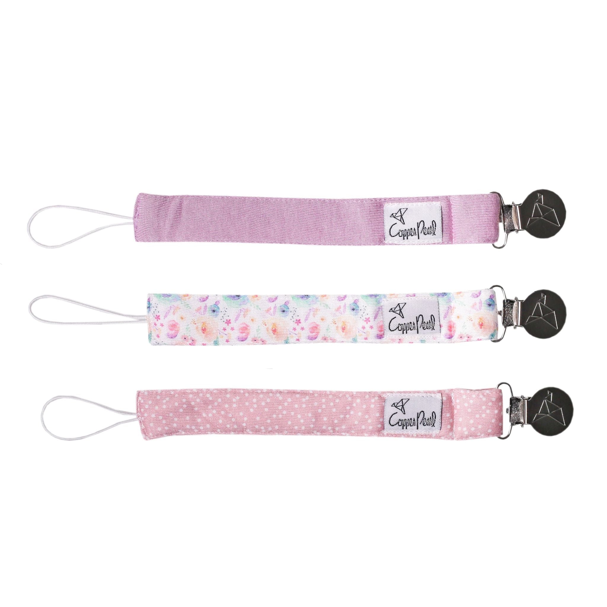 Three pink pacifier clips with floral designs on a white background. Available at Be Charmed