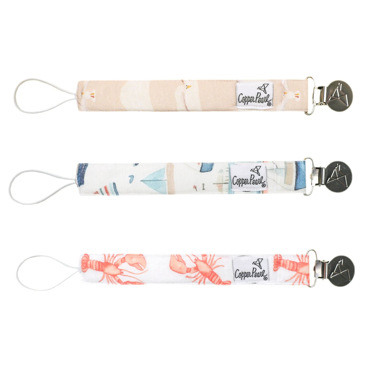 Three patterned pacifier clips on a white background, featuring different designs. Available at Be Charmed