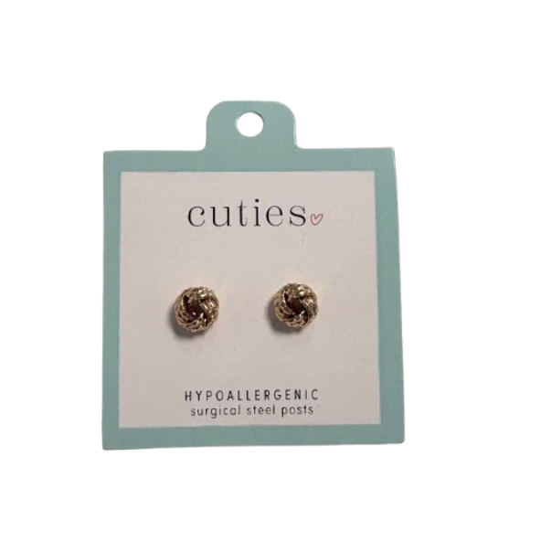 A pair of gold knot stud earrings mounted on a square display card. The card has a pale blue border and reads 'cuties' at the top and 'HYPOALLERGENIC surgical steel posts' at the bottom. Available at Be Charmed