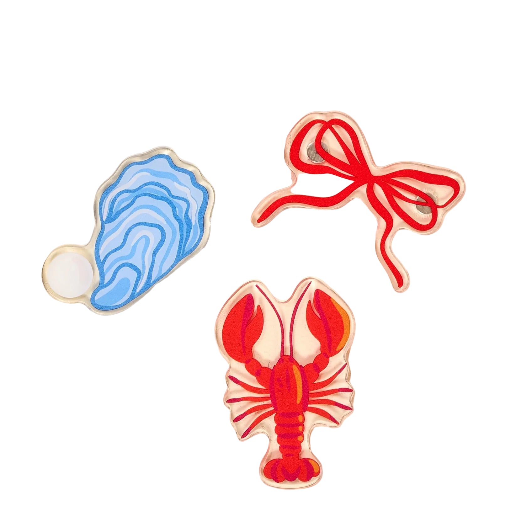 Three colorful magnets shaped like a shell, a bow, and a lobster on a beige background.. Available at Be Charmed