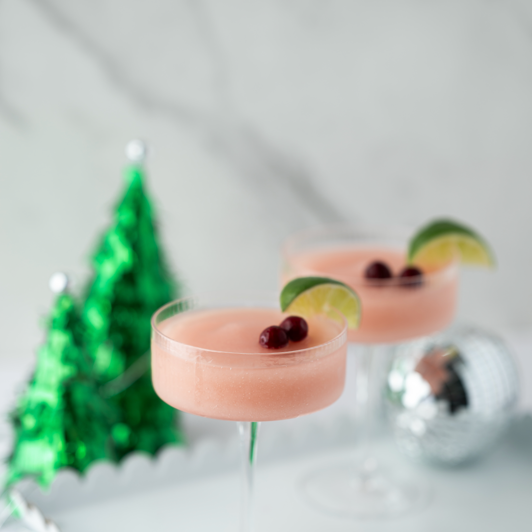 Pink cocktails with lime wedges and berries on a white tray with a festive background