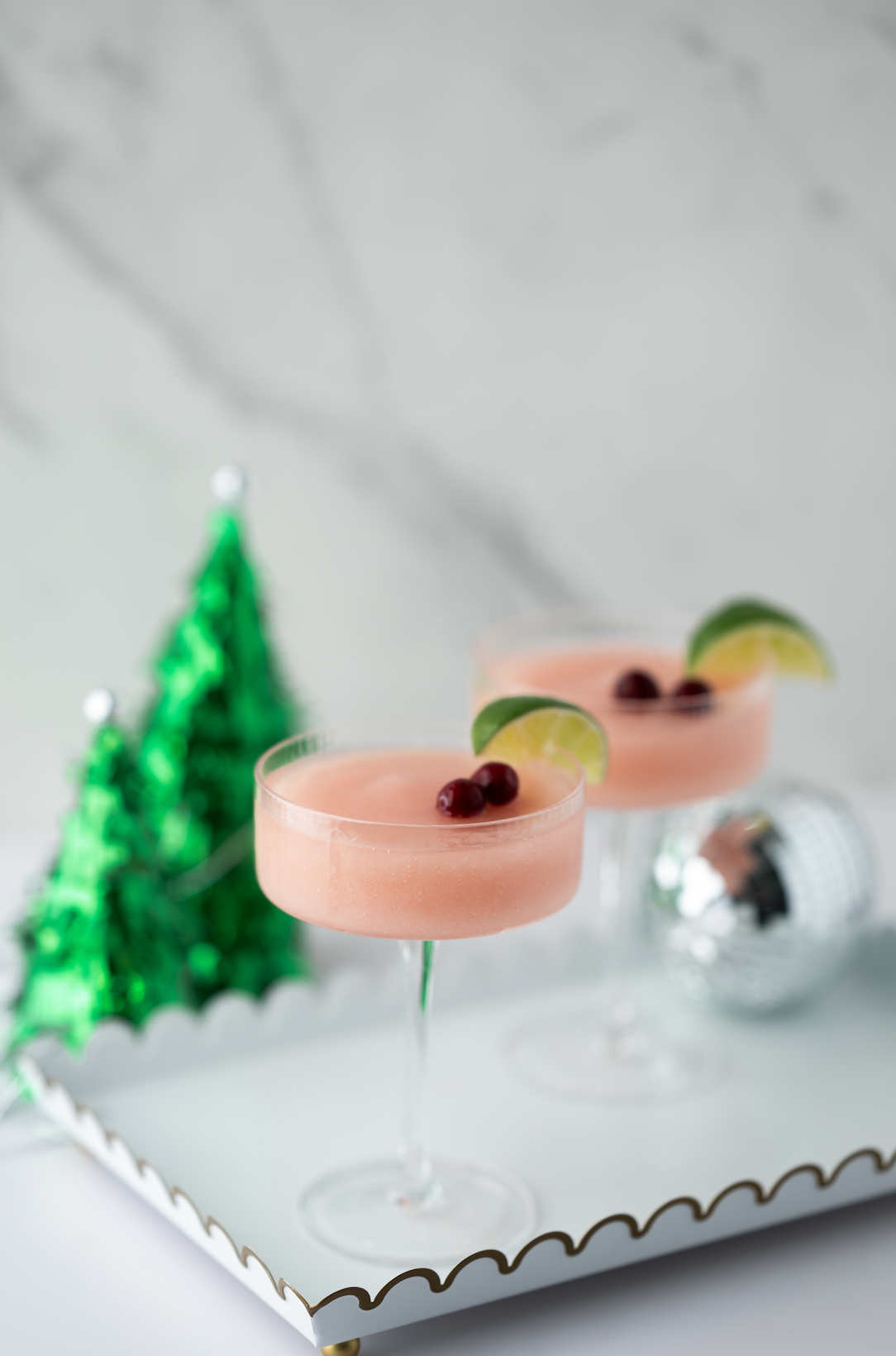 Pink cocktails with lime wedges and berries on a white tray with a festive background