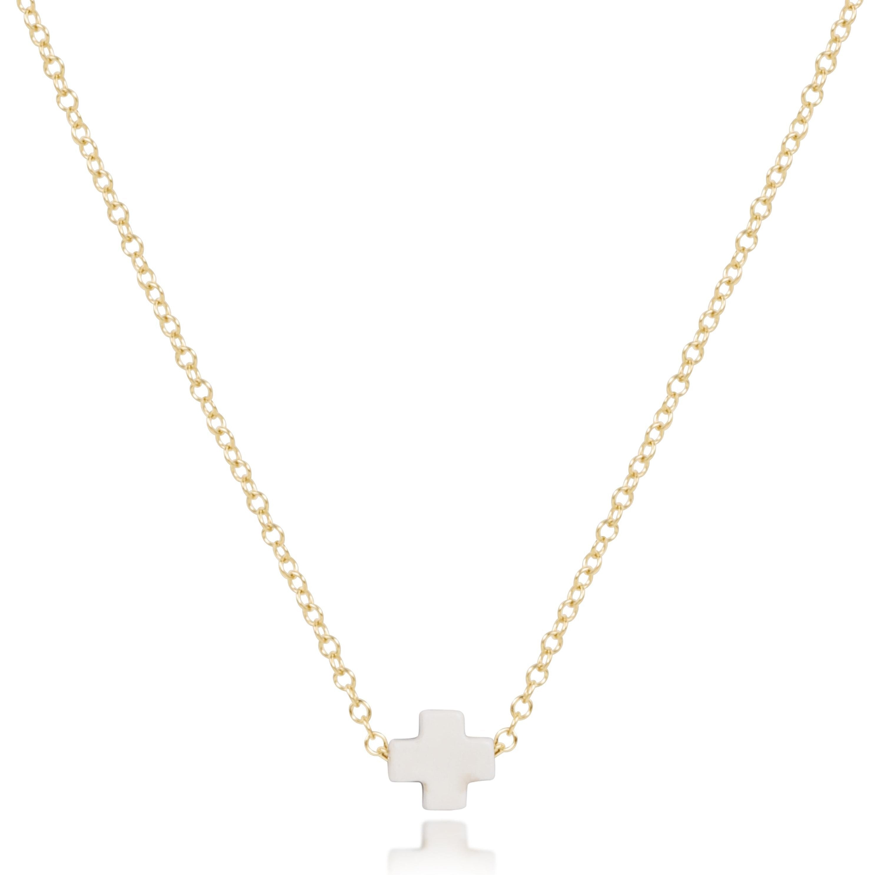 enewton Gold necklace with a off white cross pendant on a white background. Available at Be Charmed