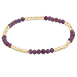 A bracelet with a series of round beads, featuring a deep ruby color with gold-filled bands. Available at Be Charmed