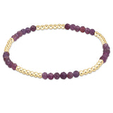 A bracelet with a series of round beads, featuring a deep ruby color with gold-filled bands. Available at Be Charmed