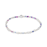 A beaded bracelet featuring white faux pearls, silver-toned beads, and small accent beads in purple, blue, and pink, arranged in a circular shape on a white background. Available at Be Charmed