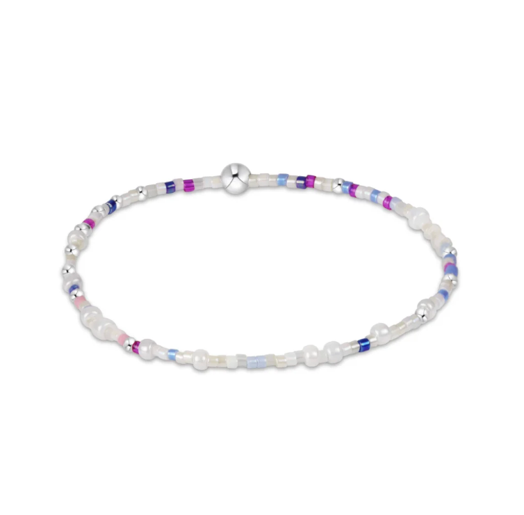 A beaded bracelet featuring white faux pearls, silver-toned beads, and small accent beads in purple, blue, and pink, arranged in a circular shape on a white background. Available at Be Charmed