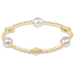 A gold-colored bracelet with a signature cross pattern and white pearls. Available at Be Charmed