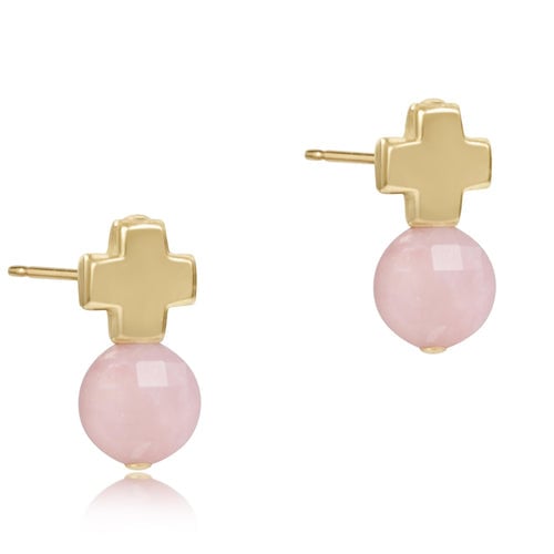 A pair of pink opal gemstone stud earrings with a gold-filled metal band and a signature cross design on the back. Available at Be Charmed