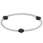 A sterling silver bracelet with navy beads, featuring a cross design, on a white background. Available at Be Charmed