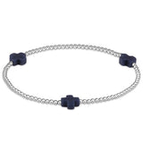 A sterling silver bracelet with navy beads, featuring a cross design, on a white background. Available at Be Charmed