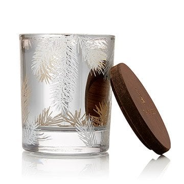 A small Frasier Fir scented candle with a silver pine needle design in a clear glass jar, accompanied by a brown lid. Available at Be Charmed