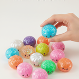 Colorful dumpling-shaped toys with a hand picking one up on a white background. Available at Be Charmed
