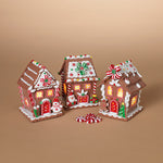 Three decorated gingerbread houses on a beige background. Available at Be Charmed