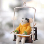 Decorative mouse ornament in a yellow sweater sitting on a swing against a blurred natural background. Available at Be Charmed