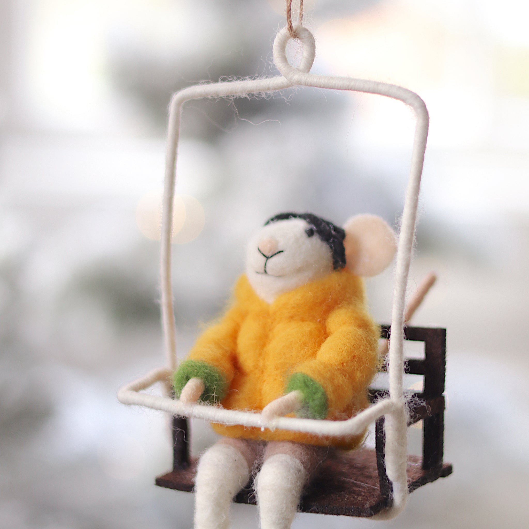 Decorative mouse ornament in a yellow sweater sitting on a swing against a blurred natural background. Available at Be Charmed
