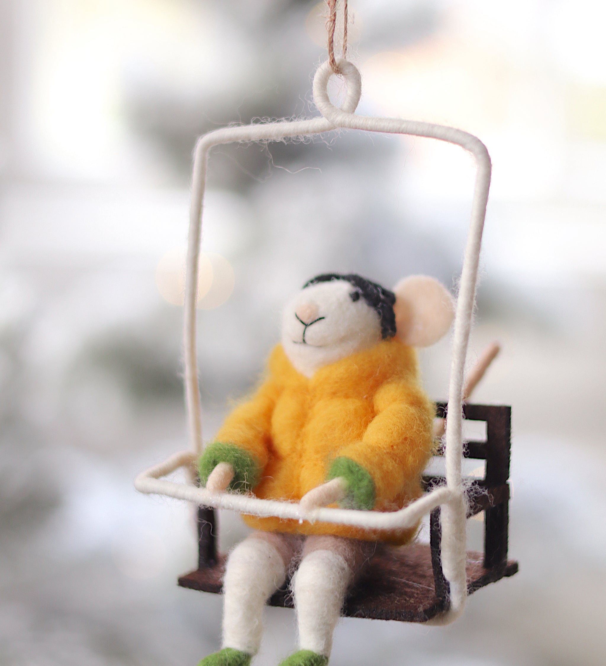 Decorative mouse ornament in a yellow sweater sitting on a swing against a blurred natural background. Available at Be Charmed