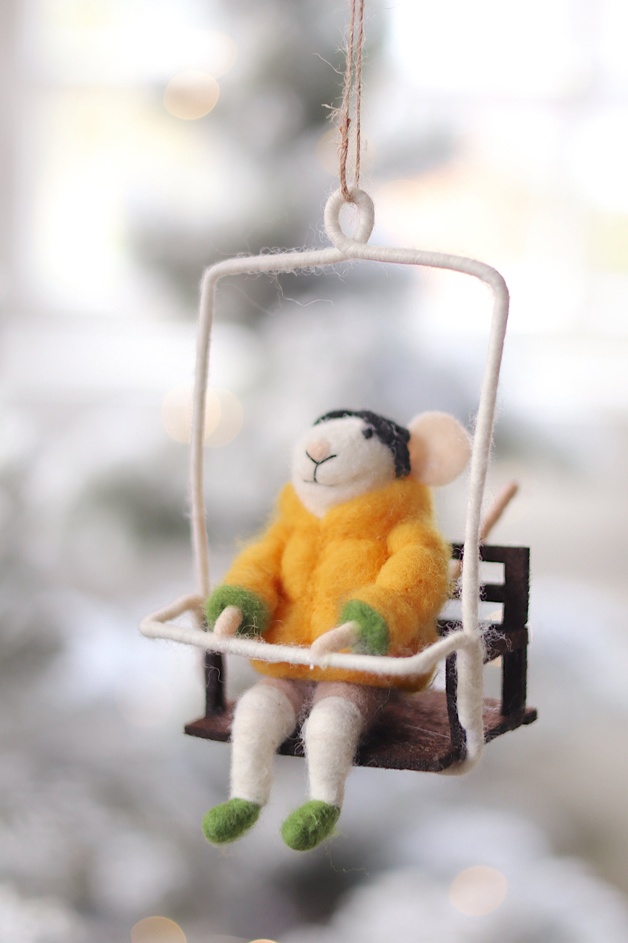 Decorative mouse ornament in a yellow sweater sitting on a swing against a blurred natural background. Available at Be Charmed