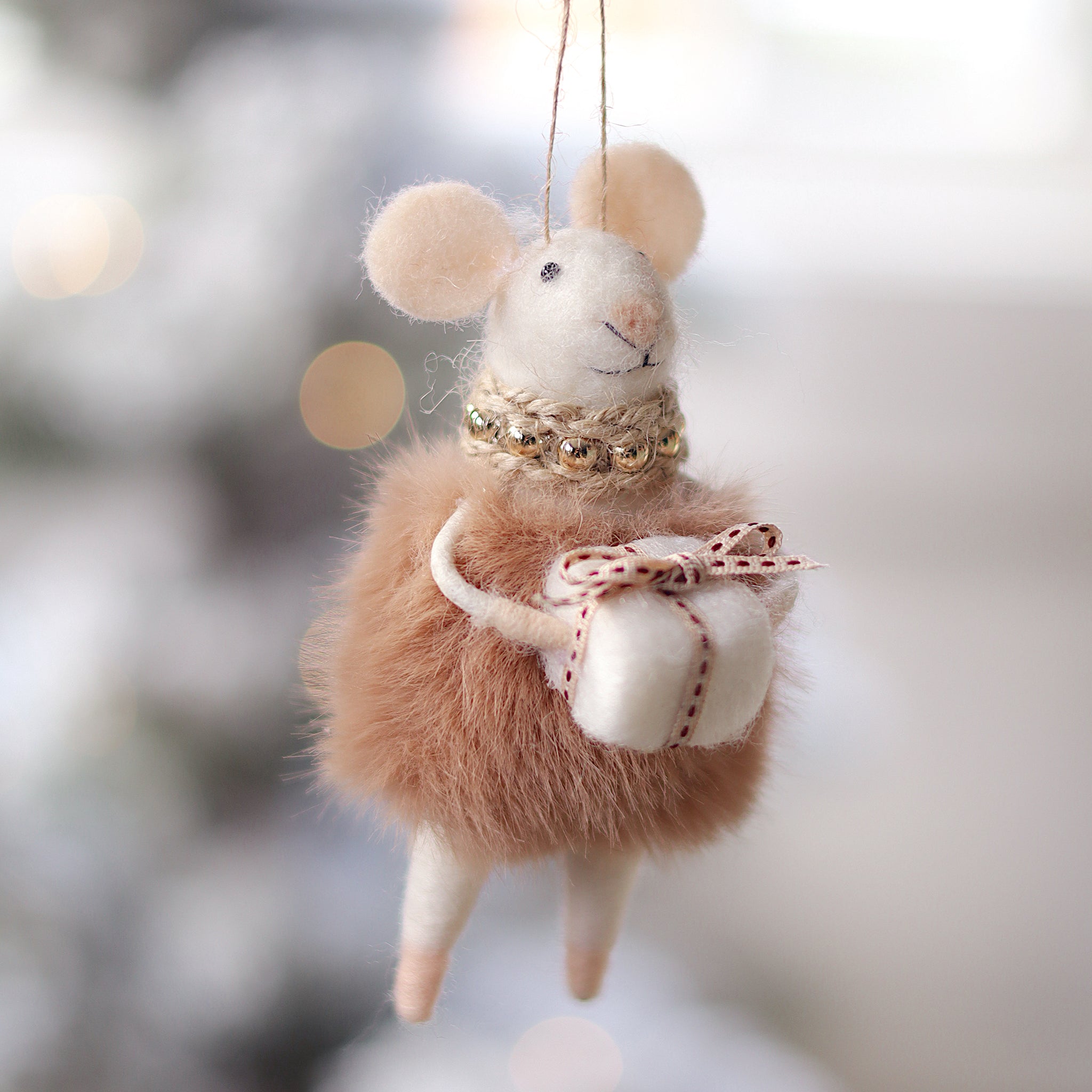 Felted mouse ornament with a bow, hanging against a blurred snowy background. Available at Be Charmed