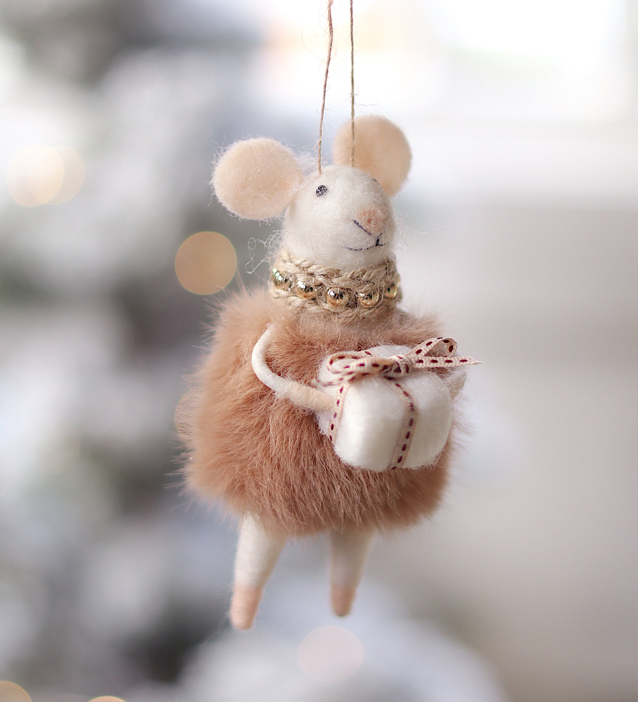 Felted mouse ornament with a bow, hanging against a blurred snowy background. Available at Be Charmed