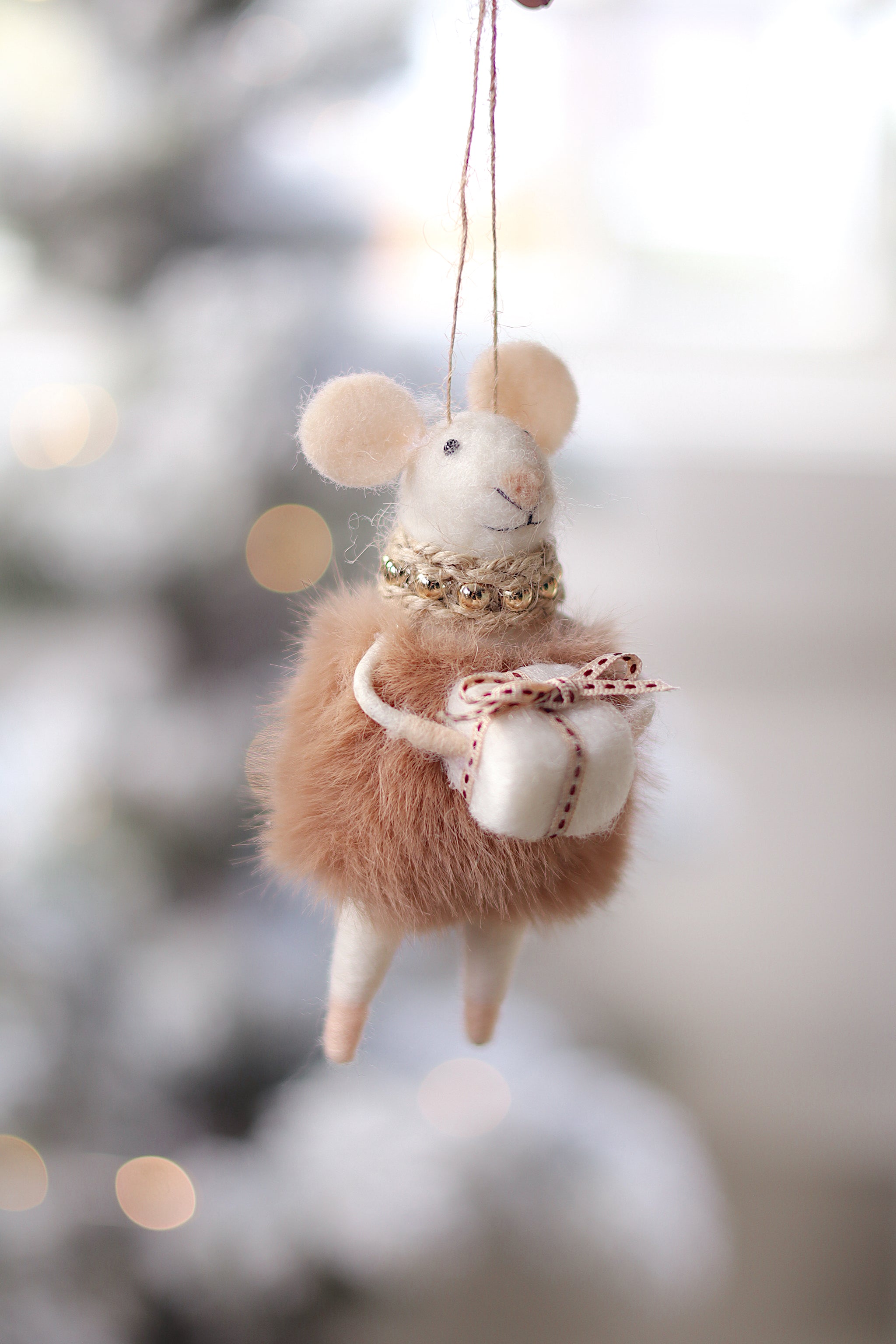 Felted mouse ornament with a bow, hanging against a blurred snowy background. Available at Be Charmed