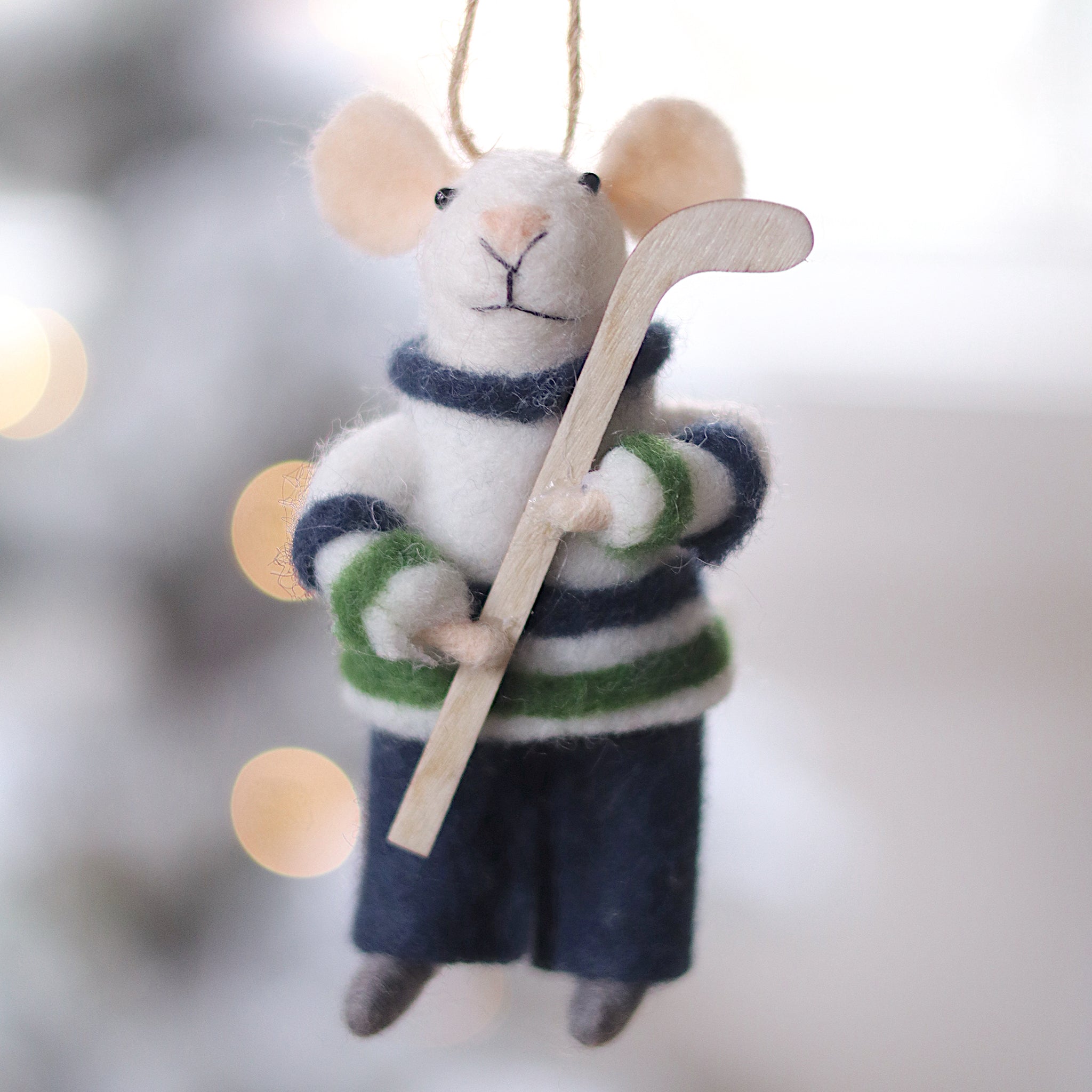 Felted mouse ornament in hockey gear hanging against a blurred snowy background. Available at Be Charmed