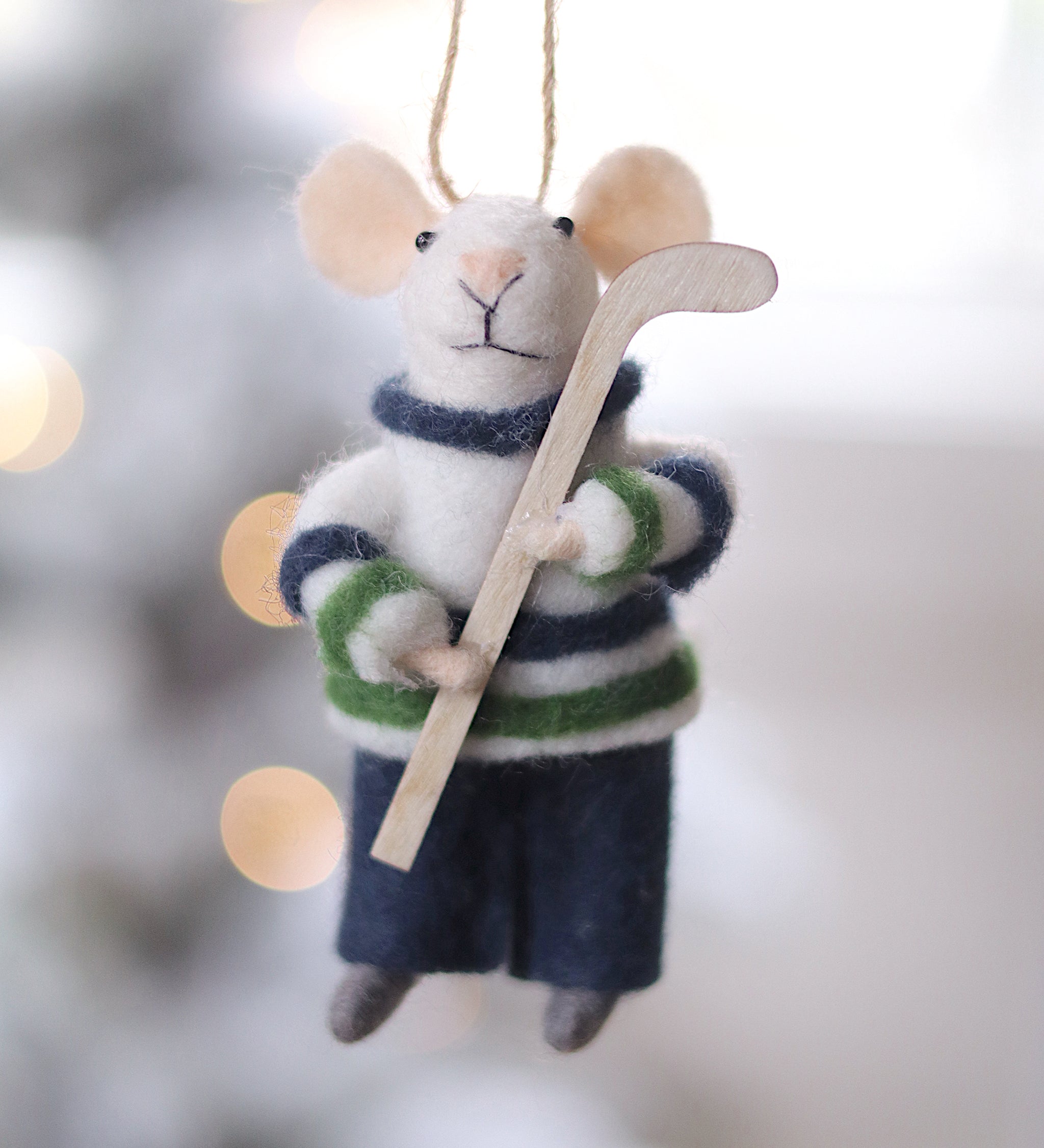 Felted mouse ornament in hockey gear hanging against a blurred snowy background. Available at Be Charmed