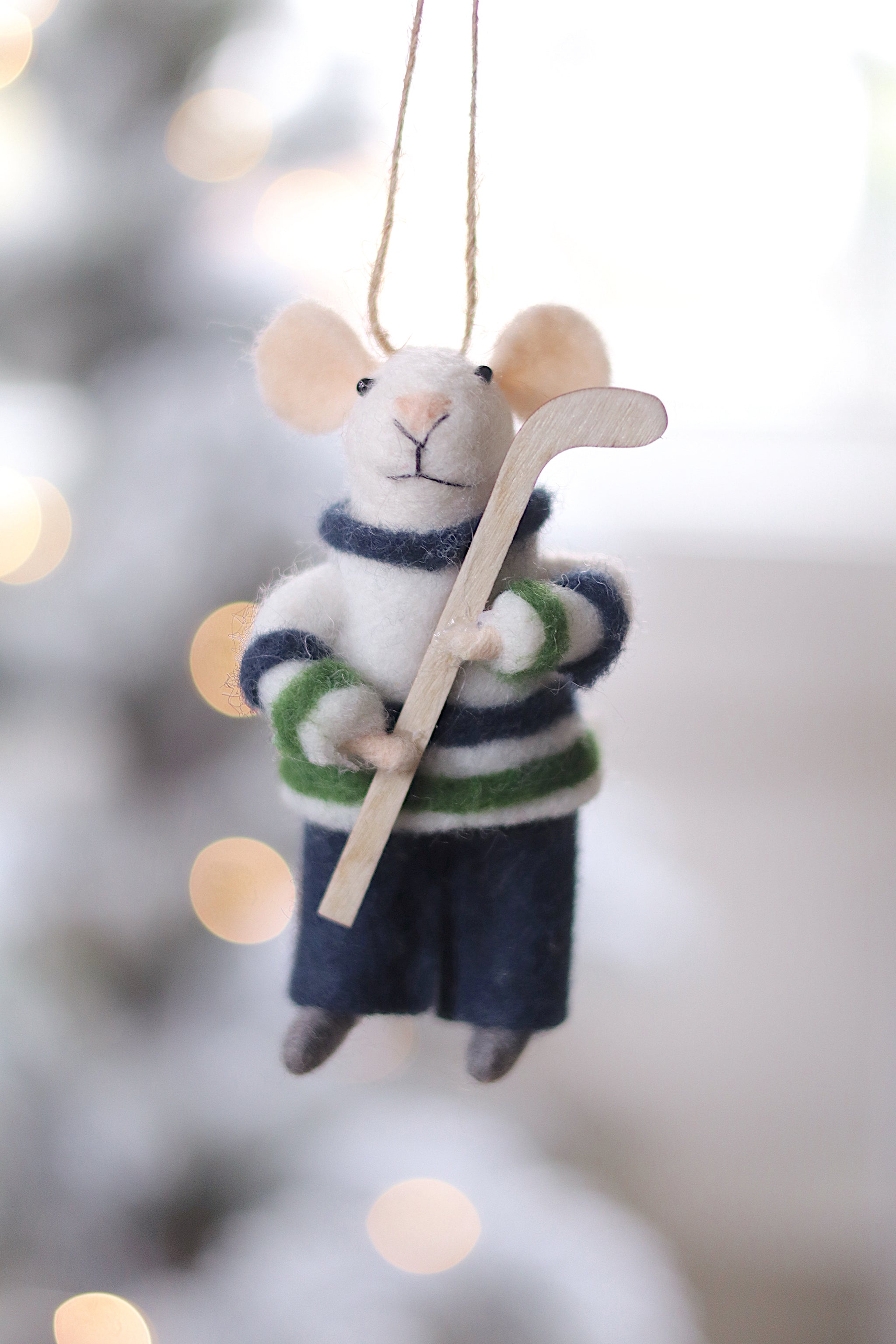 Felted mouse ornament in hockey gear hanging against a blurred snowy background. Available at Be Charmed