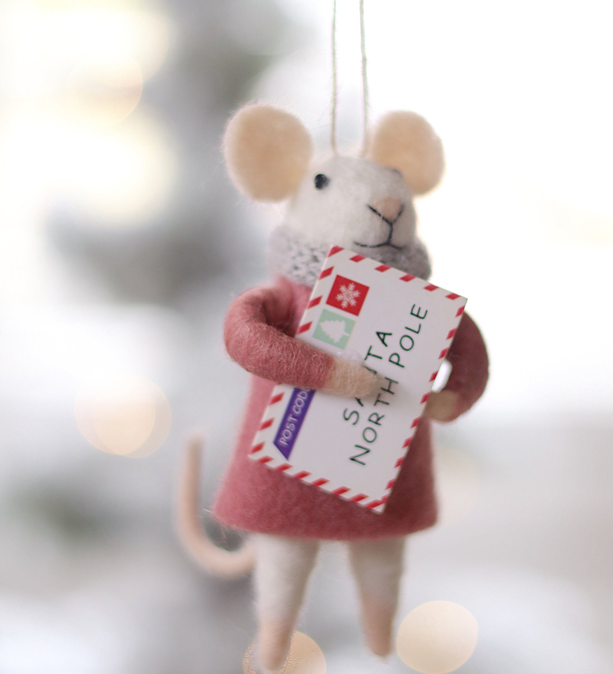 Decorative mouse ornament holding a letter with a blurred Christmas tree background. Available at Be Charmed