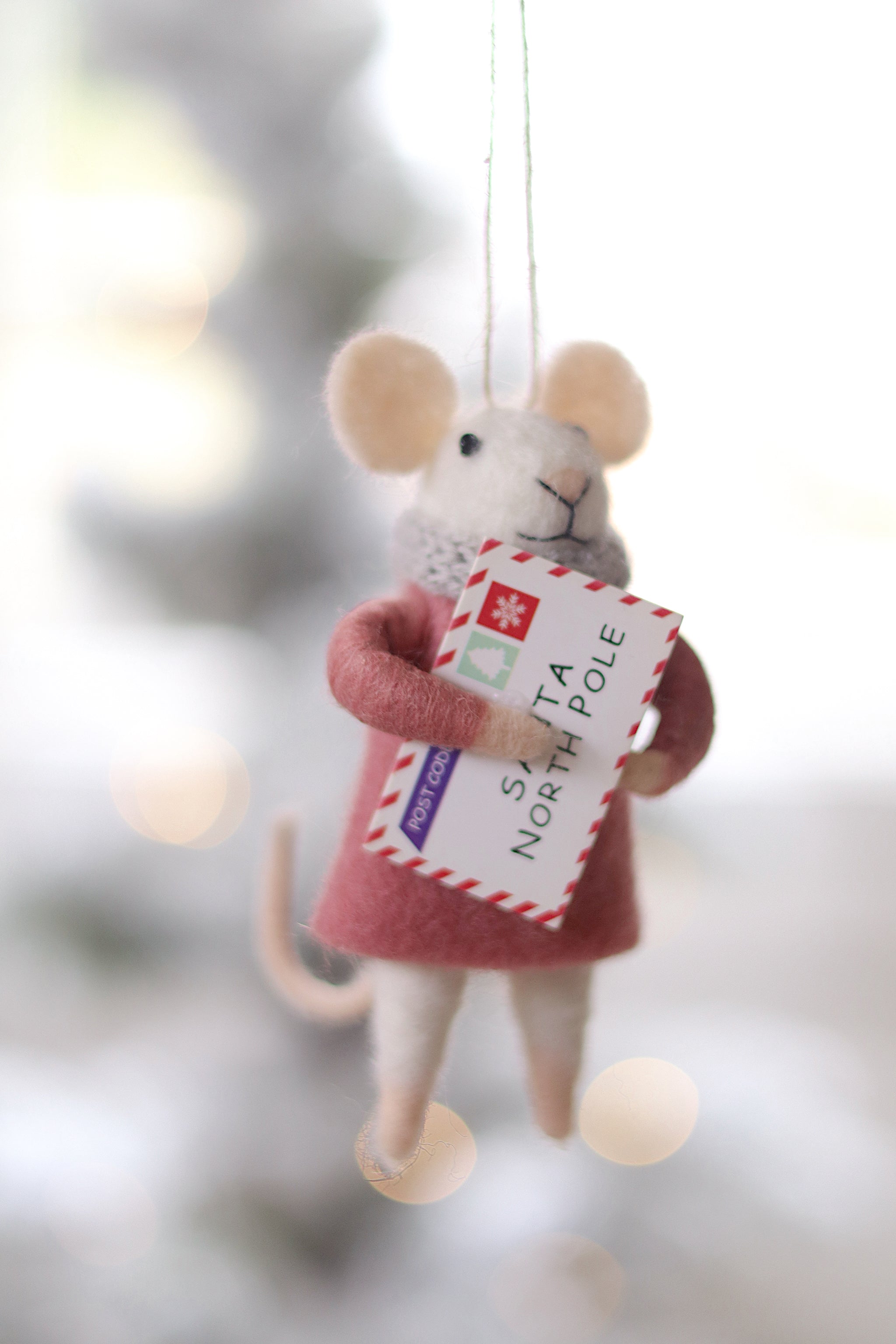 Decorative mouse ornament holding a letter with a blurred Christmas tree background. Available at Be Charmed