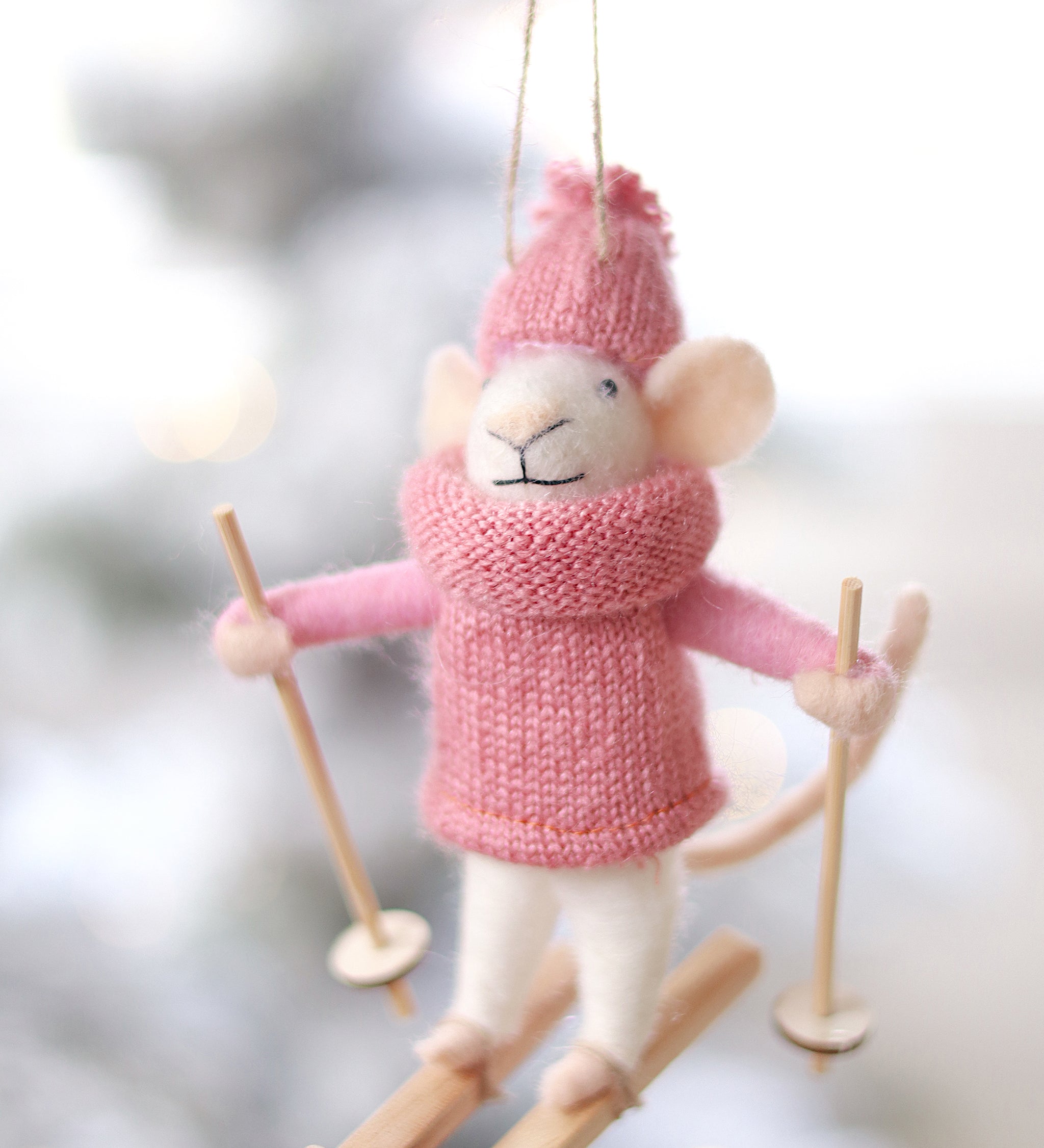 Decorative mouse ornament in pink winter clothing with skis on a blurred snowy background. Available at be Charmed