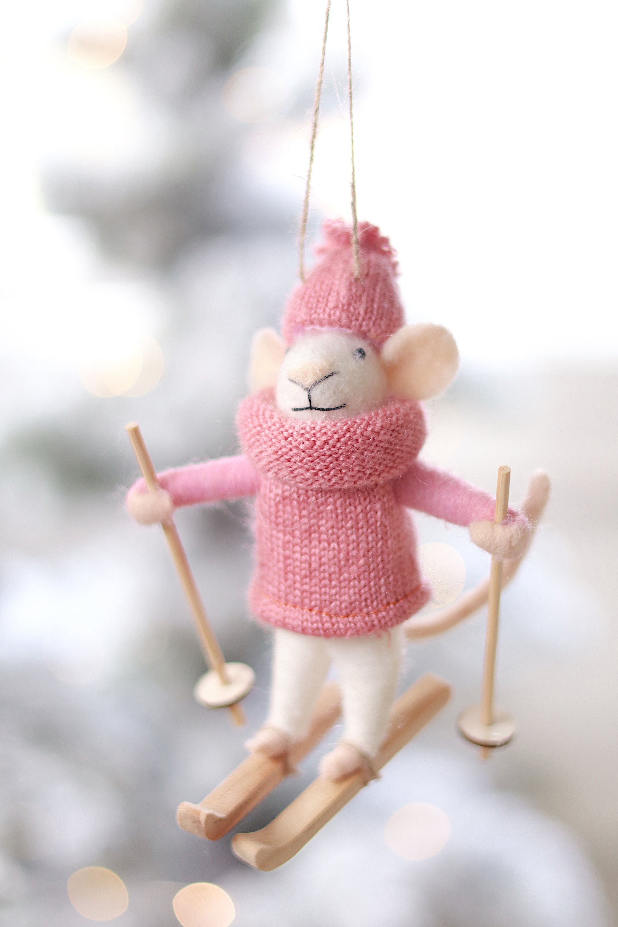 Decorative mouse ornament in pink winter clothing with skis on a blurred snowy background. Available at be Charmed