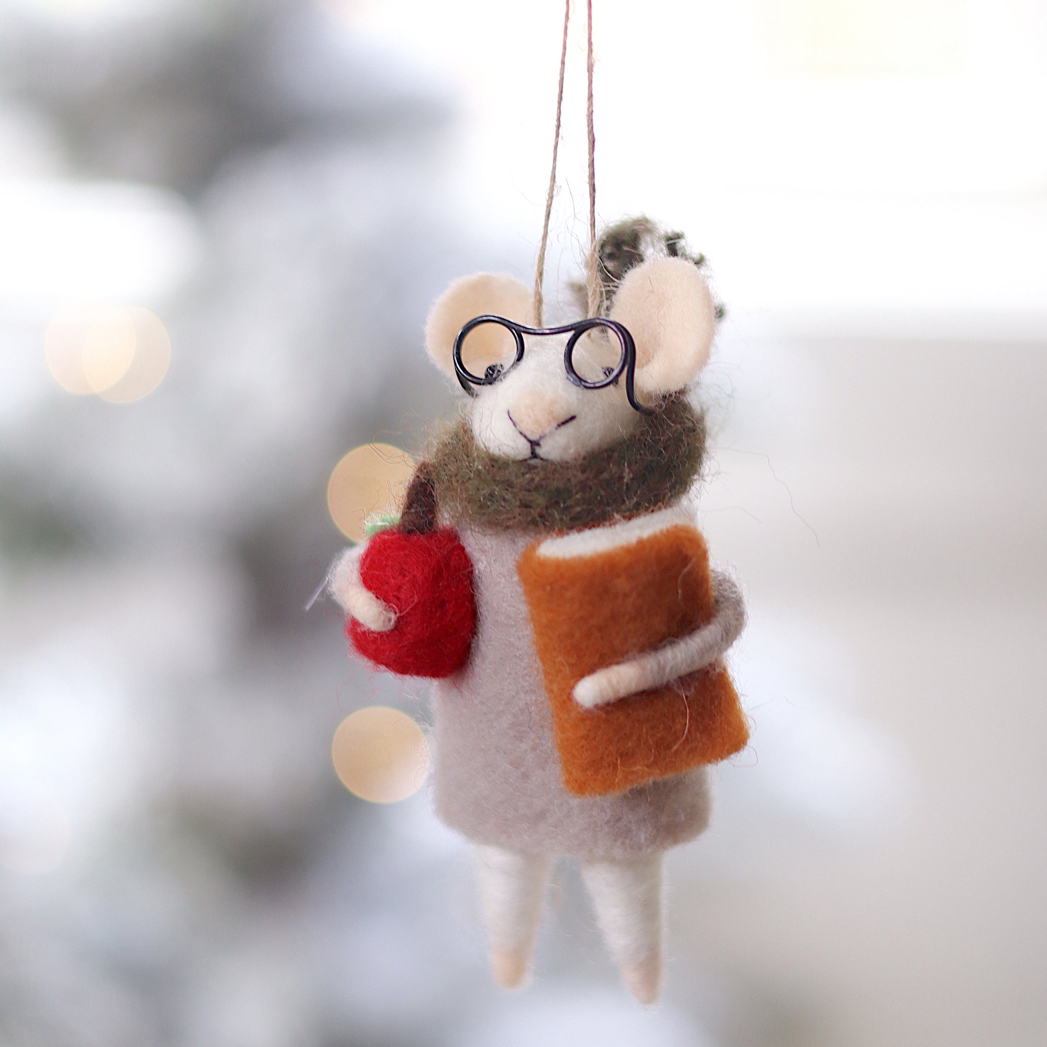 Decorative mouse ornament with glasses and a book, hanging against a blurred festive background. Available at Be Charmed